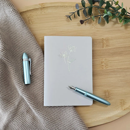 Artchemira A6 pocket journal with lotus design, in a  linen and bamboo surface with light blue pen, minimalist flat lay