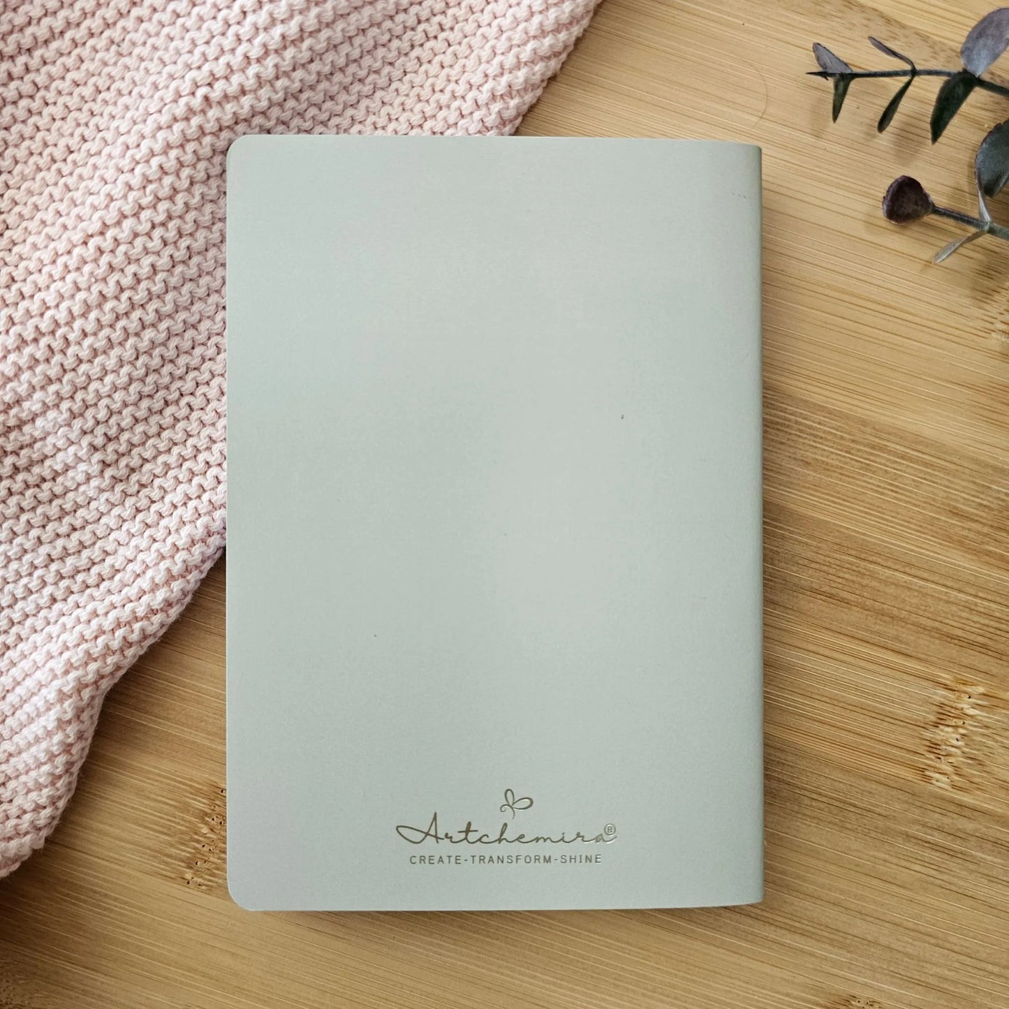 Artchemira A6 pocket journal sage mist back cover with champagne gold foil logo  detail, soft knit fabric and bamboo  desk background 