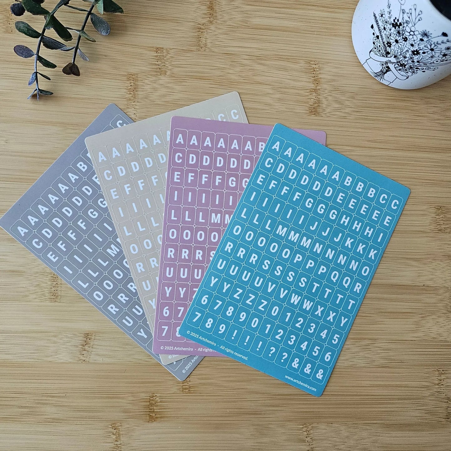 Artchemira pastel alphabet sticker sheets in cappuccino, sand, dust pink and blue  tones, flat lay
