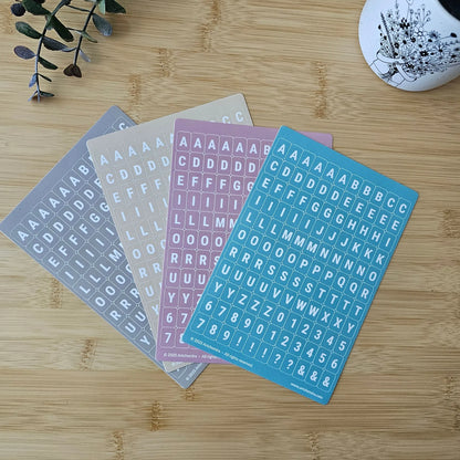 Artchemira pastel alphabet sticker sheets in cappuccino, sand, dust pink and blue  tones, flat lay
