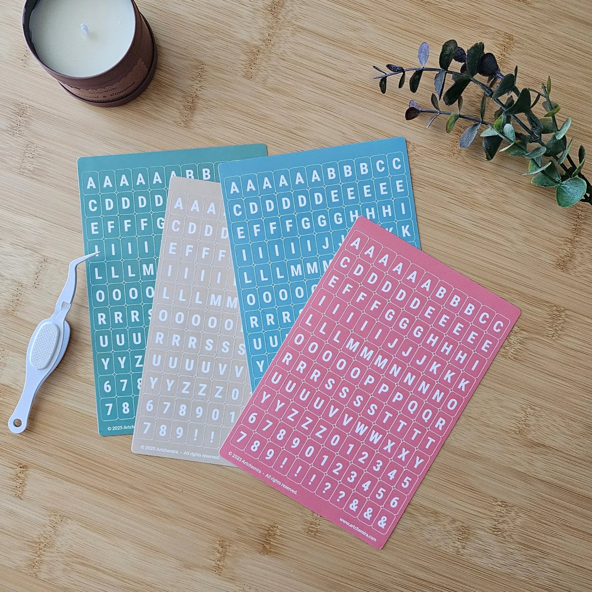 Artchemira pastel alphabet sticker sheets in green, sand, blue and coral pink tones, flat lay
