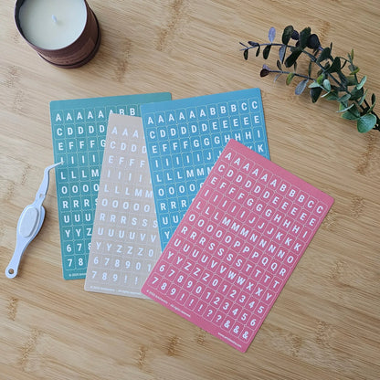 Artchemira pastel alphabet sticker sheets in green, sand, blue and coral pink tones, flat lay
