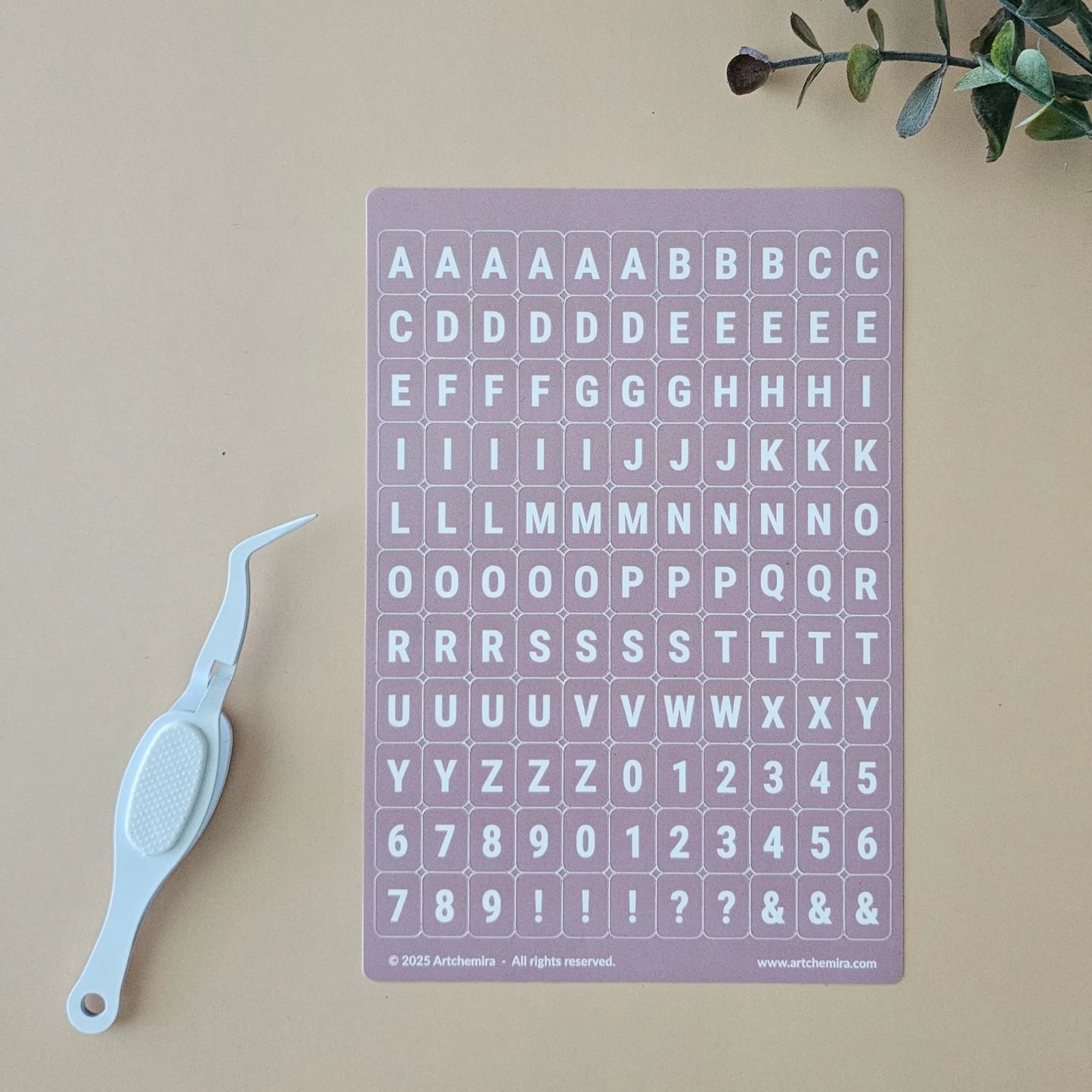 Artchemira dusty pink alphabet sticker sheet with white crafting tweezer tool
on beige surface