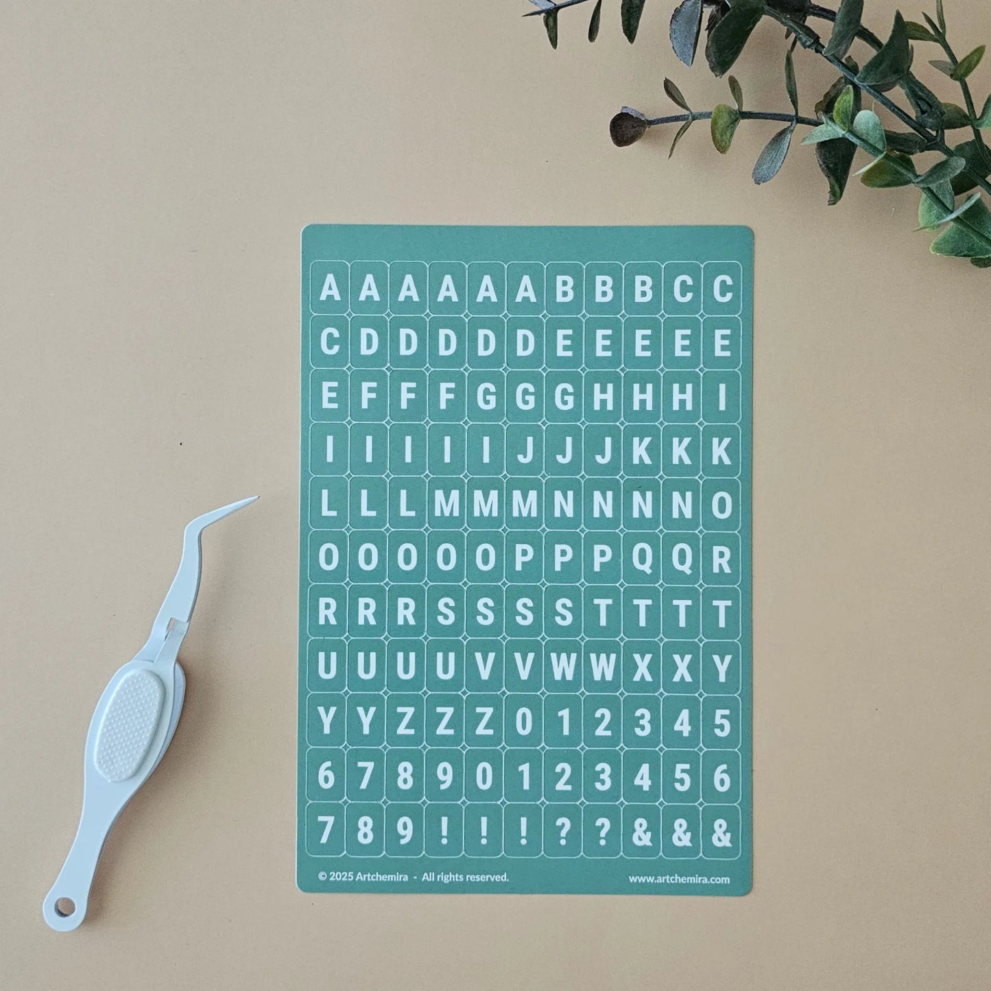 Artchemira pastel green alphabet sticker sheet with white crafting tweezer on beige surfa
