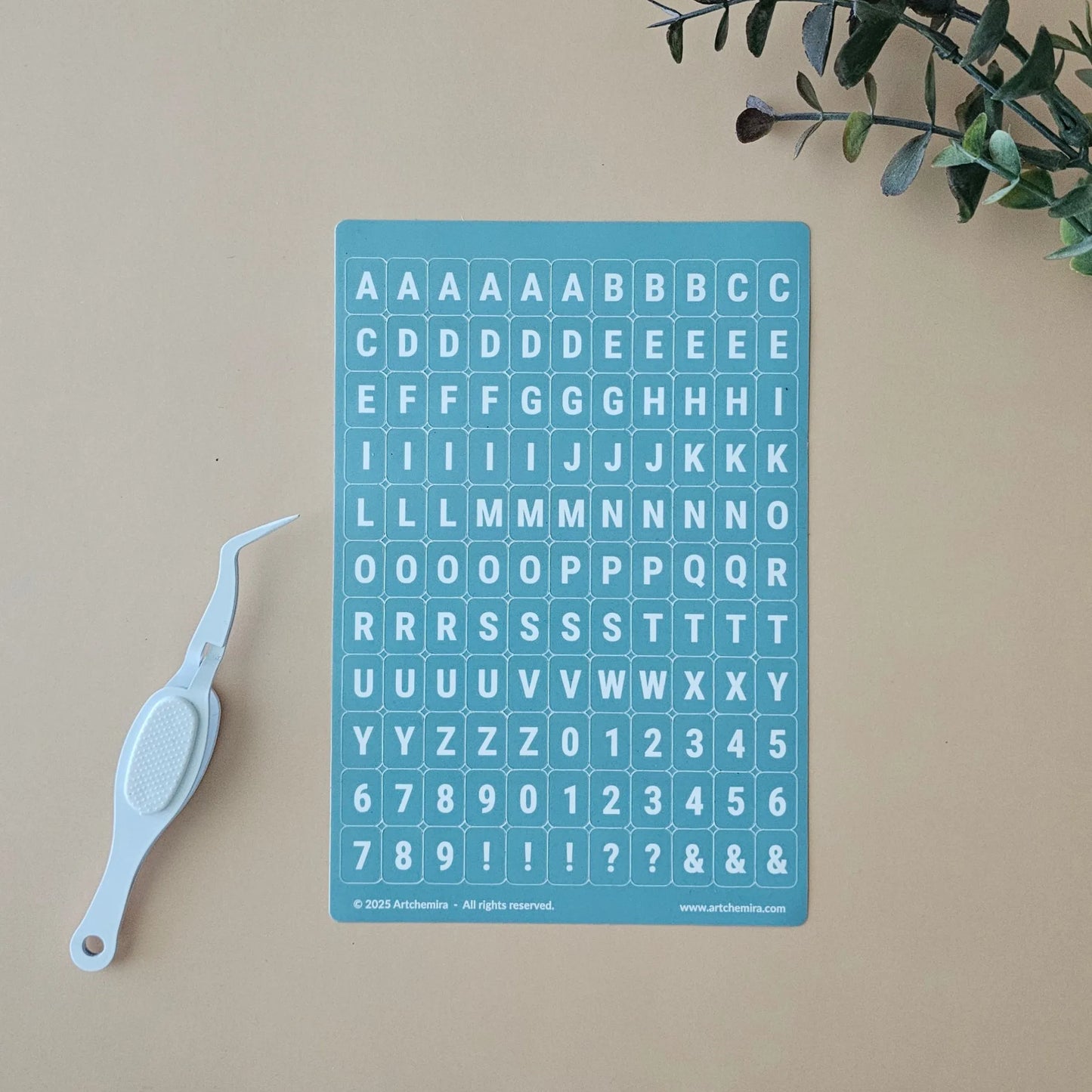 Artchemira pastel blue alphabet sticker sheet with white crafting tweezer tool on beige surface
