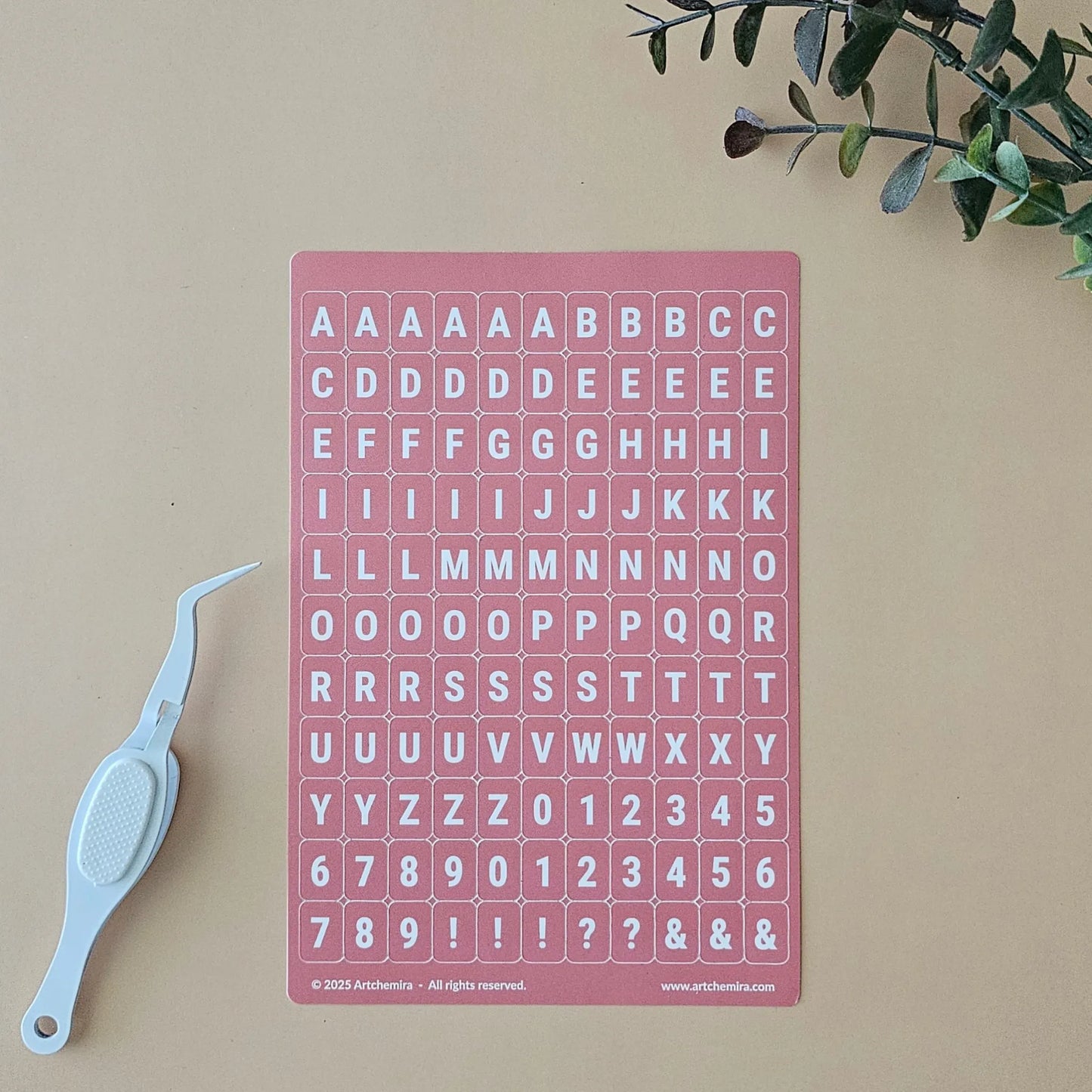 Artchemira coral rose alphabet sticker sheet with white crafting tweezer tool on beige surface