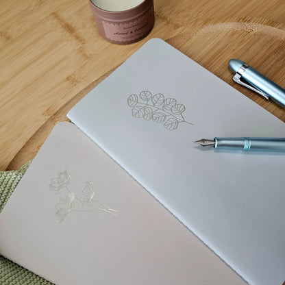 Artchemira large journal duo in sage green with champagne gold foil covers, blue pen on bamboo desk
