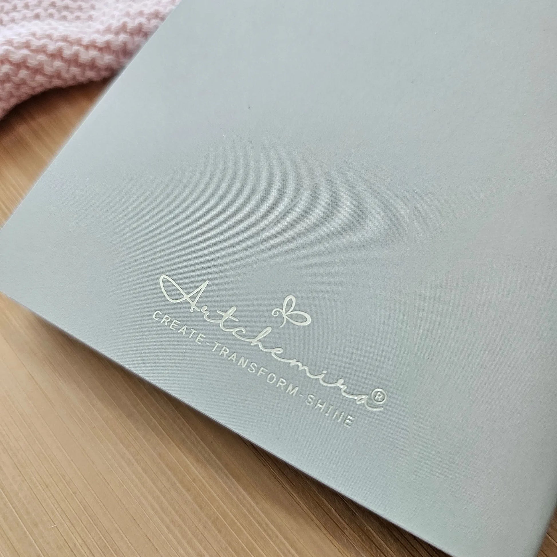 Artchemira large sage green journal back cover with gold foil logo, zoom view, on bamboo desk
