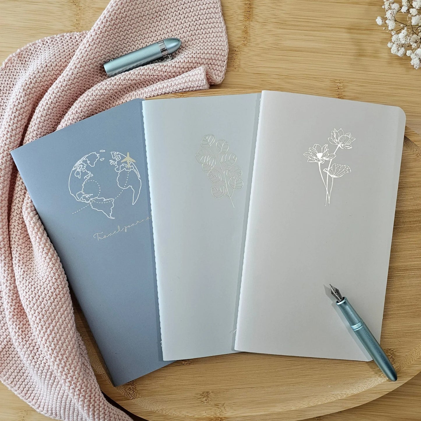 Artchemira large journal trio in cool steel, mist green , and dusty rose with  champagne gold foil covers featuring Globe and Plane Eucalyptus and Lotus on bamboo desk