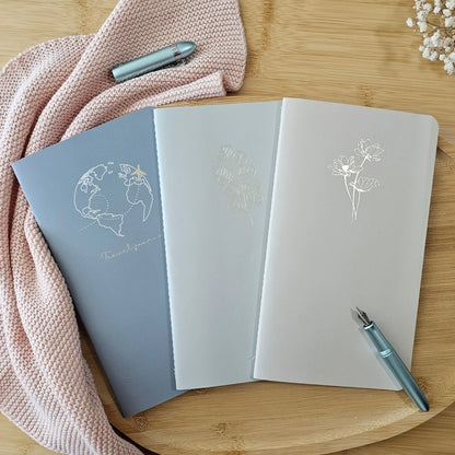 Artchemira large journal trio in cool steel, mist green , and dusty rose with  champagne gold foil covers featuring Globe and Plane Eucalyptus and Lotus on bamboo desk
