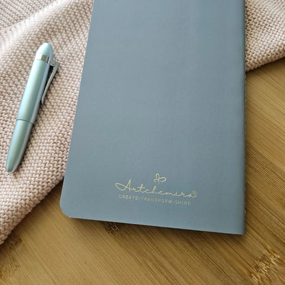 Artchemira large travel journal in cool steel with gold globe and plane foil on bamboo desk
